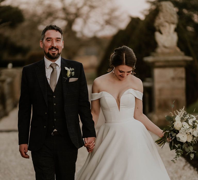 Groom in a dark blue suit and with a dark brown satin tie with the bride in a pleated wedding dress 