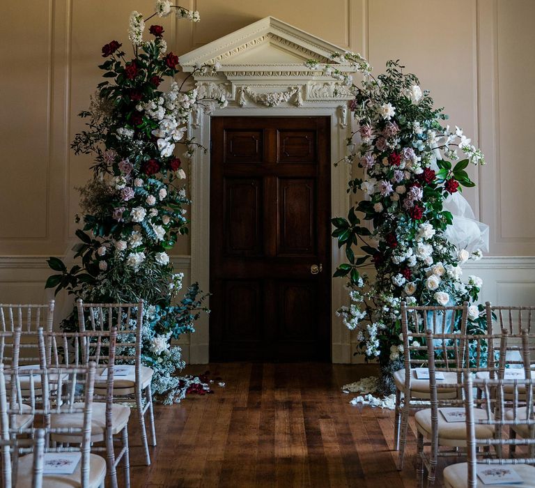 Floral archway filled with white and red roses and green foliage in front of wooden door at Findon Place 