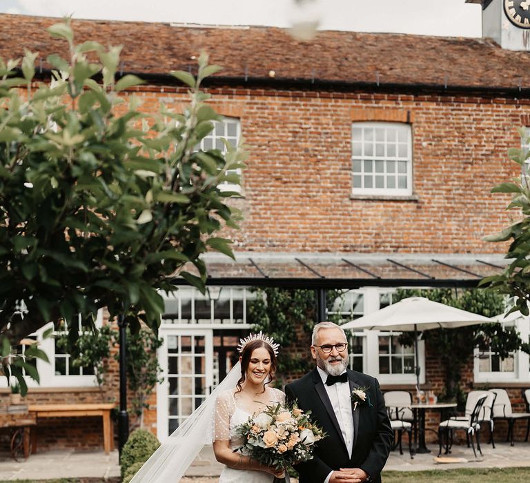 Father of the bride in black tie walks the bride in a dotted wedding dress down the aisle for the outdoor ceremony 