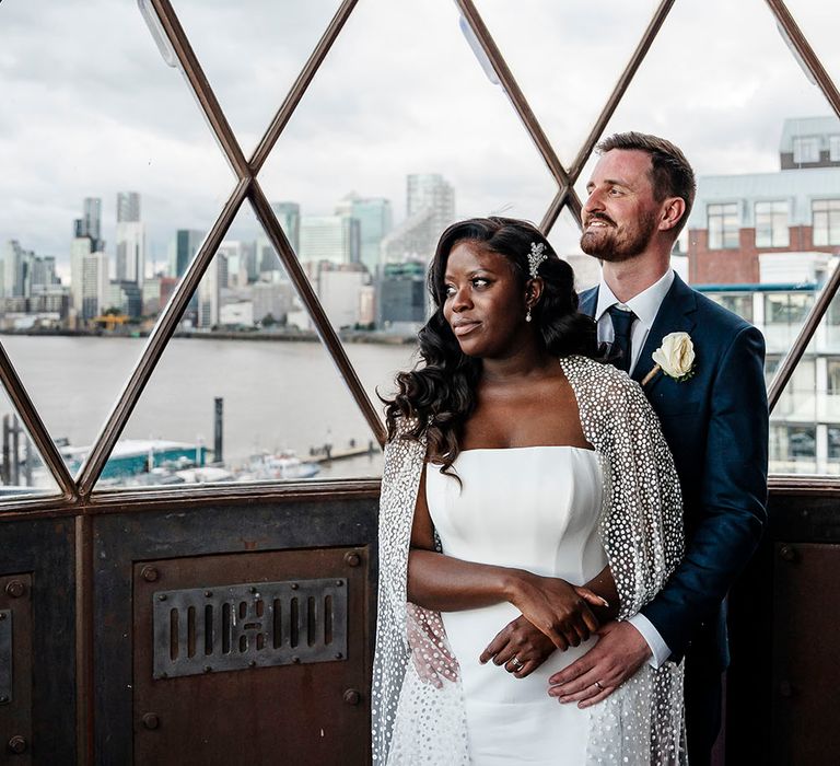 Groom wraps his arms around his bride as they stand at the top of lighthouse during couples portraits 