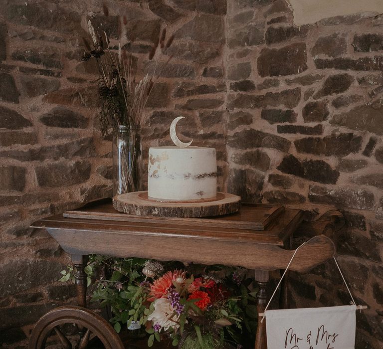 Naked wedding cake with white frosting and moon cake topper on wooden table 