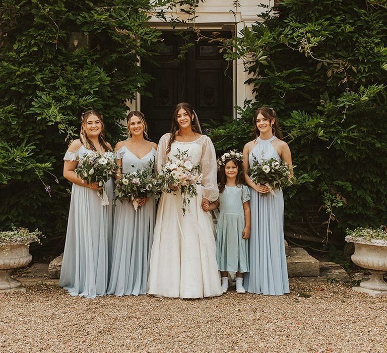 Bridesmaids in pale blue dresses with a flower girl in a blue dress and the bride in a balloon sleeve dress 