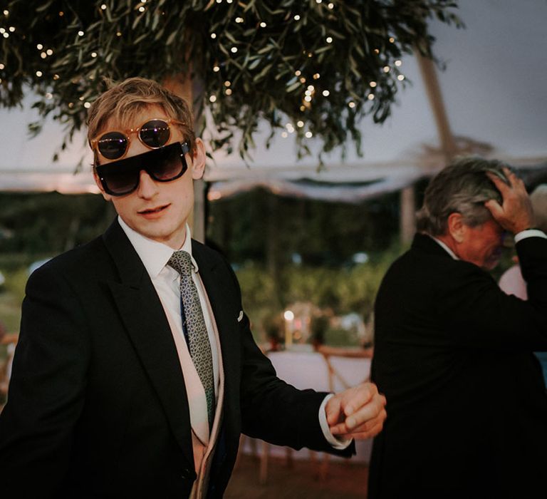 Groomsmen in morning suit and pink waistcoat wearing two pairs of sunglasses 