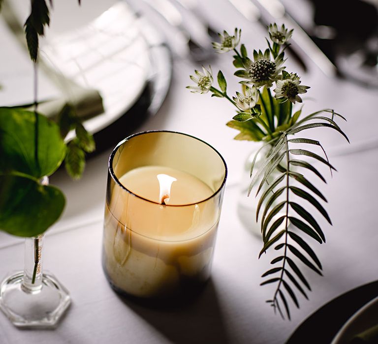 Small floral arrangements on white tablecloth complete with lit candle 