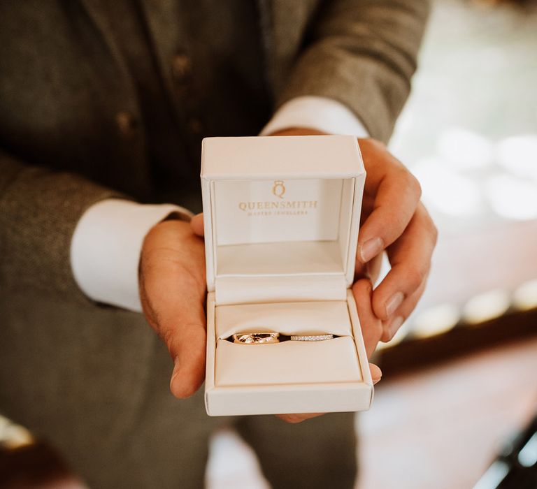 White ring box holding the groom's gold wedding ring and bride's diamond gold wedding band 