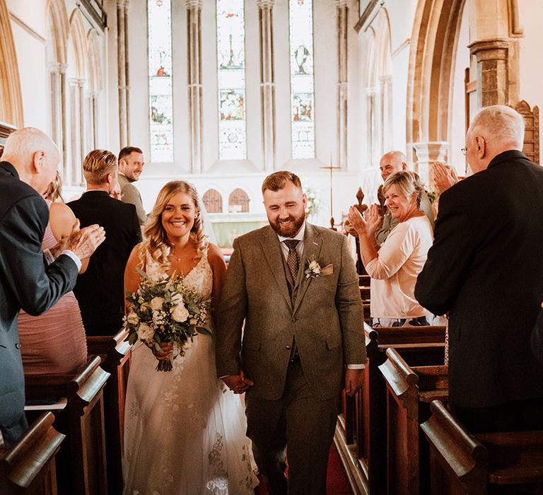 Bride and groom walk back down the aisle as the wedding guests stand and applaud 