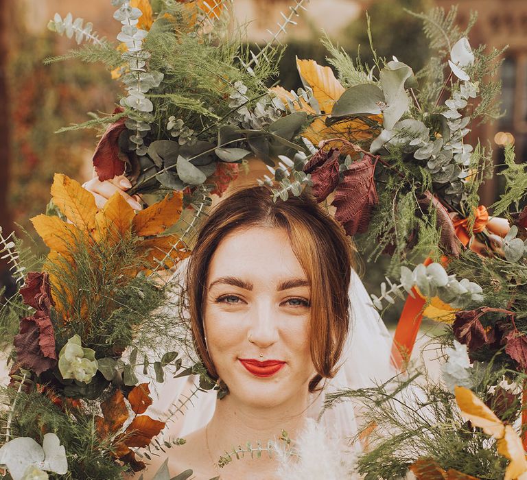 Bride wears red lipstick and is surrounded by colourful Autumnal flowers 