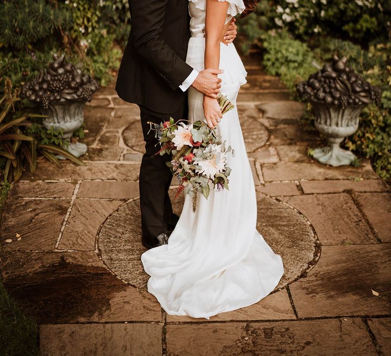 Groom in classic black tuxedo with black bowtie kissing bride in v-neck satin wedding dress with sheer butterfly sleeves on the cheek