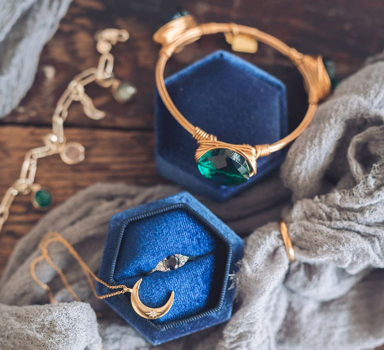 The bride's jewellery with a gold bangle bracelet with emerald stone and moon necklace with blue hexagonal ring box with sapphire engagement ring 