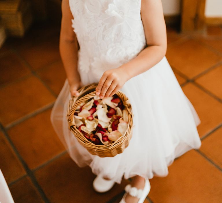 Blonde flower girl wears flower crown and carries wicker basket filled with colourful petals 