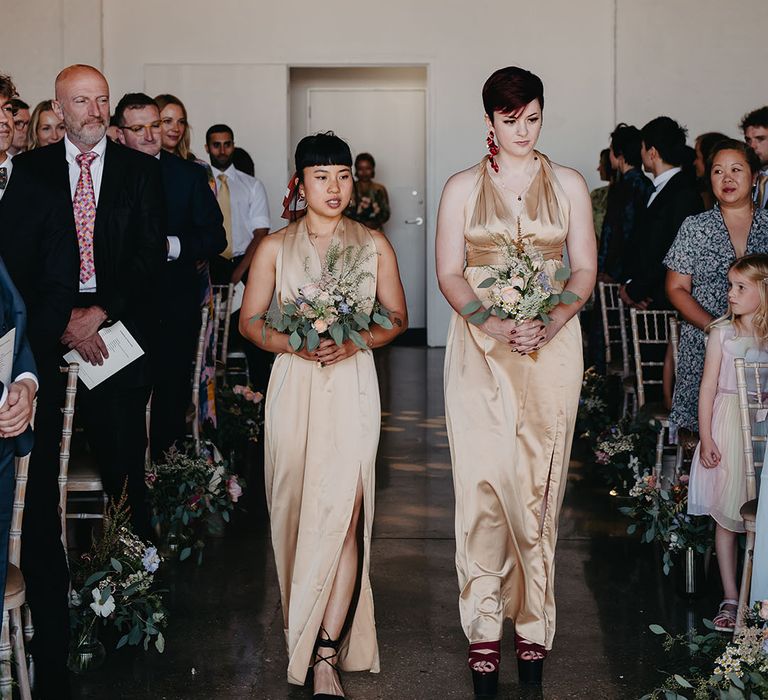 Bridesmaids in halter neck gold bridesmaid dresses walk down the aisle 