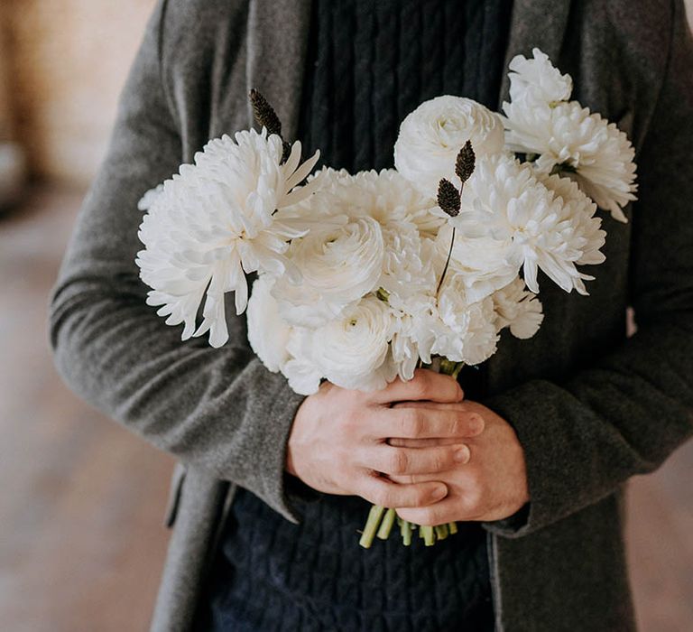 Groom in dark grey suit holding bouquet with white roses, white peonies and white chrysanthemums