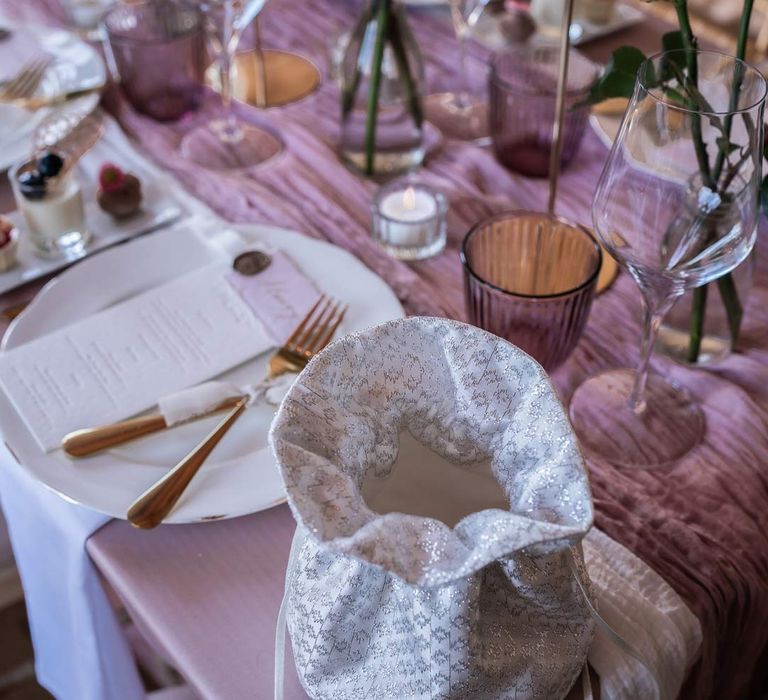 Shimmery lilac and white bridal bag on modern wedding tablescape with lavender tablecloth, lilac tulle table runner, blush garden rose centrepieces, tea light candles and tapered candles