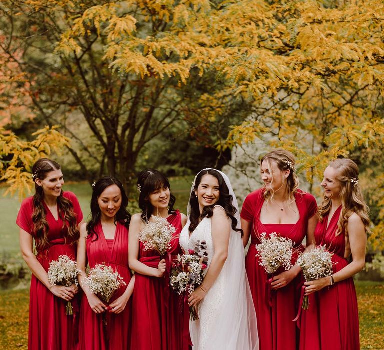 Bridesmaids in mismatched red bridesmaid dresses holding baby's-breath bouquets with red ribbon standing with bride in sleeveless lace wedding dress and church length red ombre veil - red lace wedding dress