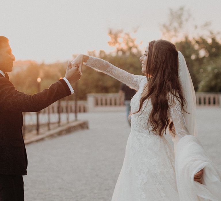 Golden hour couples wedding photoshoot - bride in lace long sleeve Pronovias wedding dress and church-length veil and groom in classic black tuxedo 