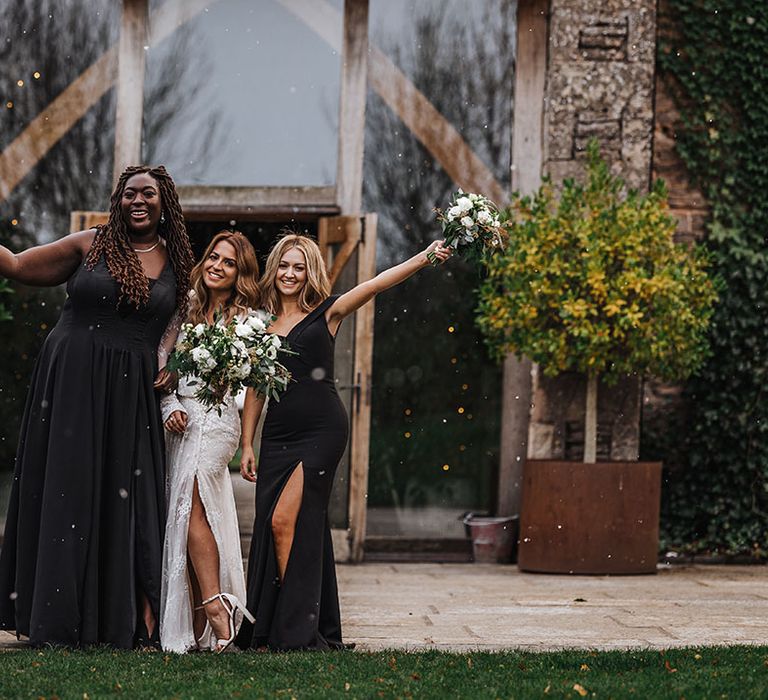 Bridesmaids in black bridesmaid dresses posing with the bride for snowy November wedding