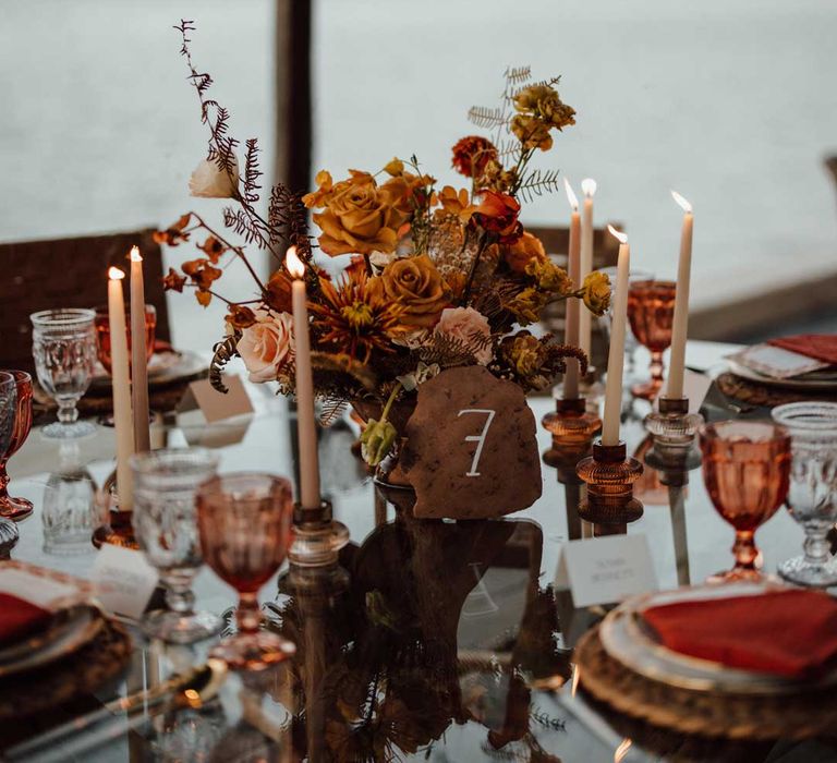 Rustic wedding tablescape with burnt orange dried roses, dried flower and foliage floral centrepieces, wooden slate wedding table numbers, light orange tapered candles and burnt orange wedding napkins 