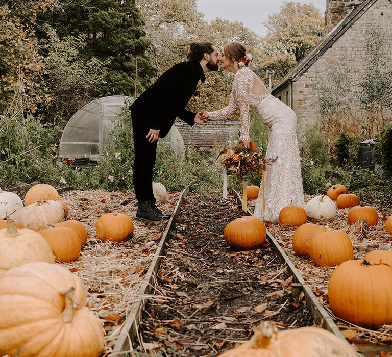 Pumpkin patch wedding in autumn with the groom in an all black velvet suit and bride in a boho long sleeve wedding dress 