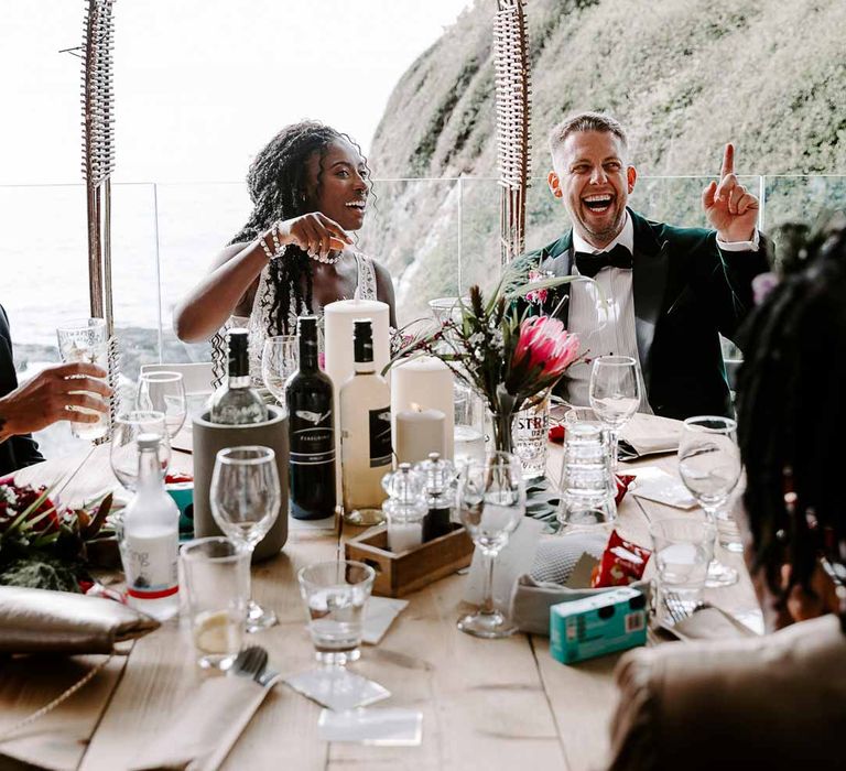 Bride in sleeveless lace Pronovias wedding dress sitting with groom in bottle green velvet blazer and bowtie at classic rustic wedding tablescape 