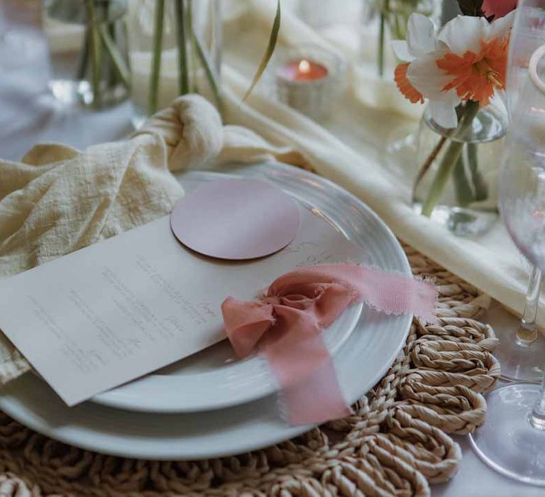 Classic white crockery on burlap wedding place mat with minimalist wedding stationery, dusky pink ribbon and yellow wedding napkins 