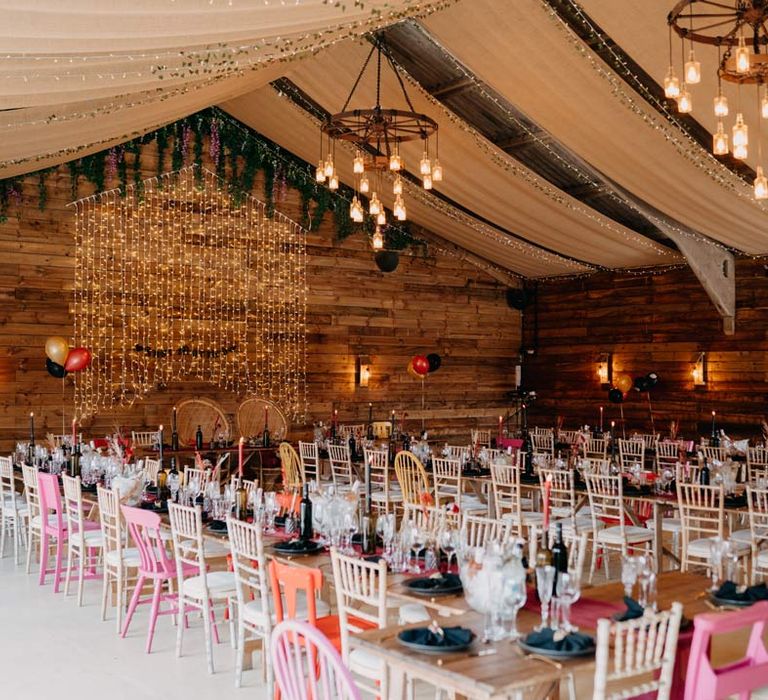 Rock and roll wedding tablescape with deep red wedding table runner, black plates, black napkins, gold cutlery, red tapered candles in black wine bottles, and red white and black pampas grass wedding centrepieces at Southlands Barn