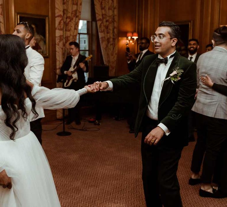 Bride in off the shoulder layered tulle wedding dress dancing with groom in bottle green velvet grooms suit, black bowtie and chic boutonniere at Inner Temple Hall 