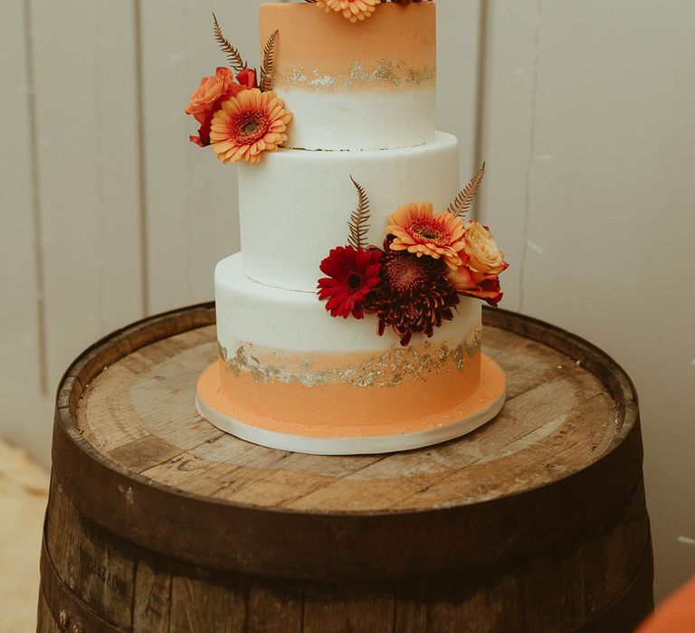 Three tier white and orange ombre iced wedding cake with gold flakes and orange cake topper 