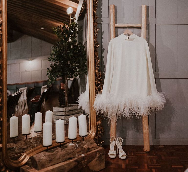 Bride's Taller Marmo high neck long sleeve short feather wedding dress hanging up with Jimmy Choo shoes 