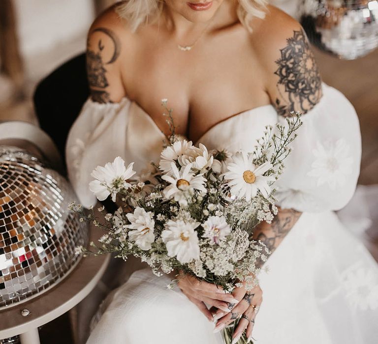 Bride in sweetheart off the shoulder wedding dress with tattoos holding daisy bouquet 