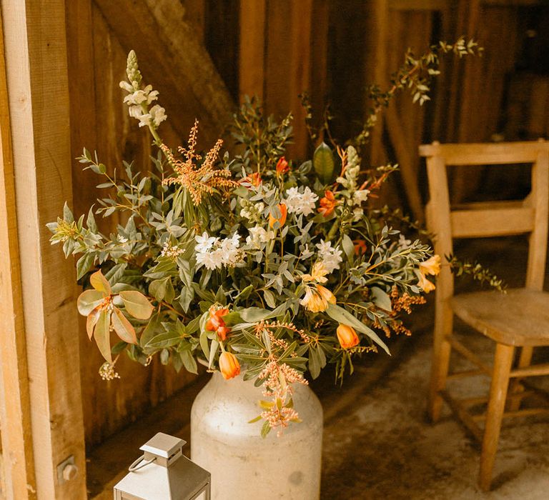 Vintage milk churn with arrangement of orange wedding flowers in 