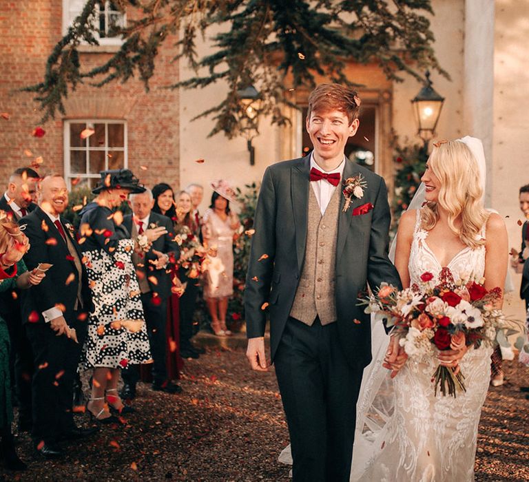 Bride holding red and white wedding bouquet with white anemones walking out with the groom for confetti exit 