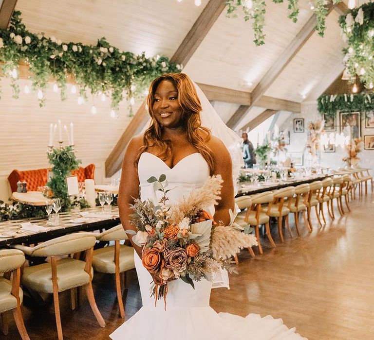 Bride wearing strapless mermaid fishtail wedding dress holding autumnal bouquet 