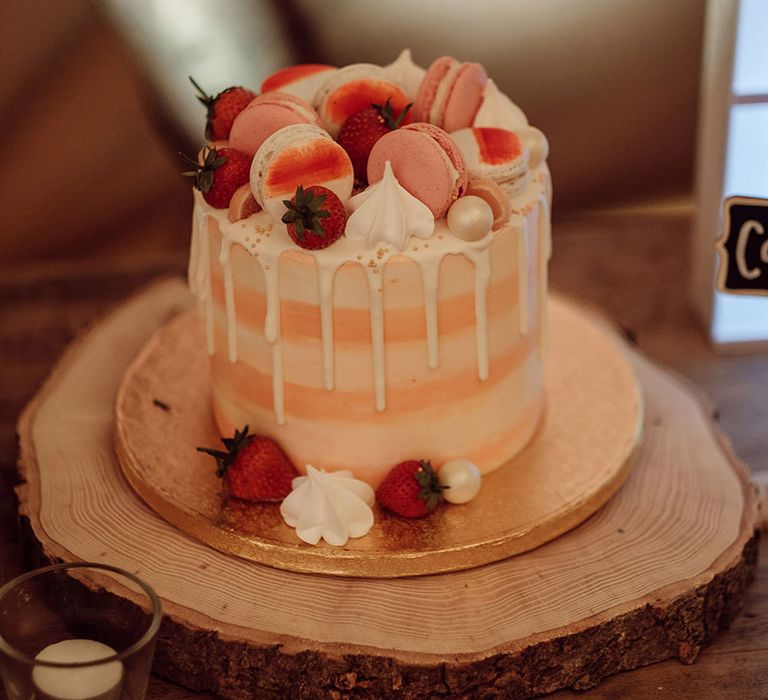 Peach and white wedding cake with white drip icing with macarons, strawberries, meringues and edible pearls 