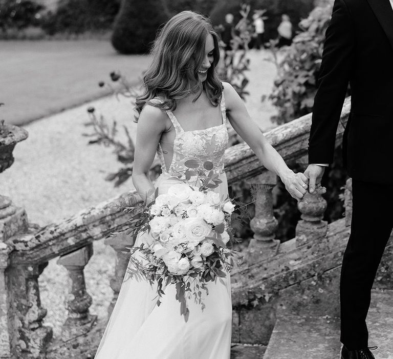 The bride carries a white wedding bouquet up the stairs of the wedding venue 