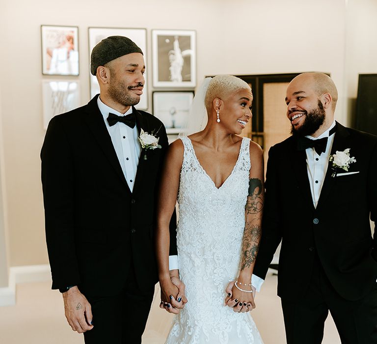 Bride in lace wedding dress with two wedding guests in black tuxedos 