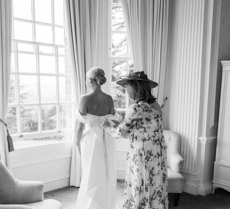 Black and white image of a mother of the bride in a floral dress helping the bride with her bow