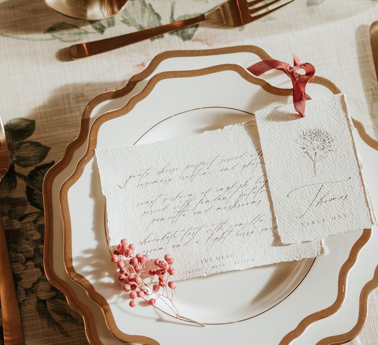 Traditional white and gold place setting with aged wedding stationery and gold cutlery 