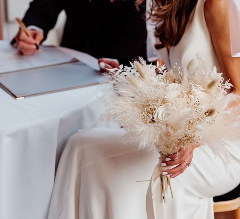 Bride carrying dried flower white wedding bouquet with bunny grass for winter wedding 