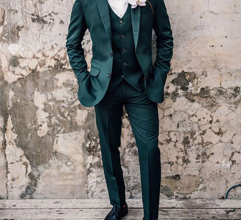 Groom in three piece dark green wedding suit with orchid buttonhole and orange bow tie 