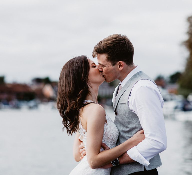 Bride & groom kiss on wedding day with river in the background 