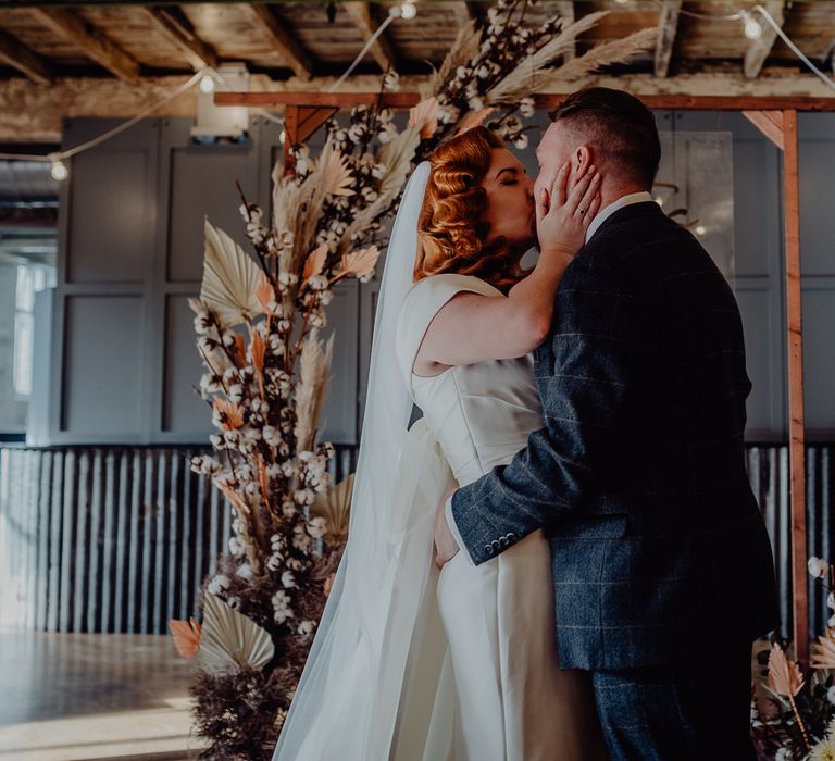 Bride with vintage wedding hair kissing her groom at the dried flower altar