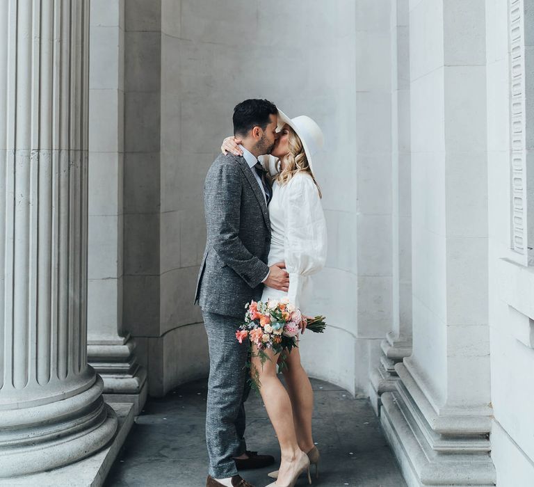 Bride and groom kissing Marylebone London wedding, bride wearing short wedding dress and bridal hat 