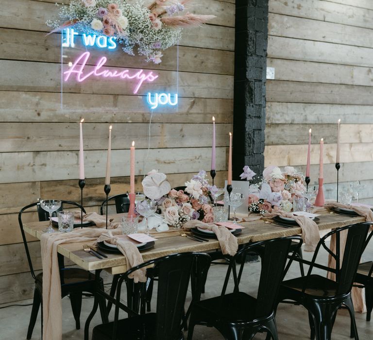 Tablescape with pink and purple wedding decor including taper candles and neon sign backdrop