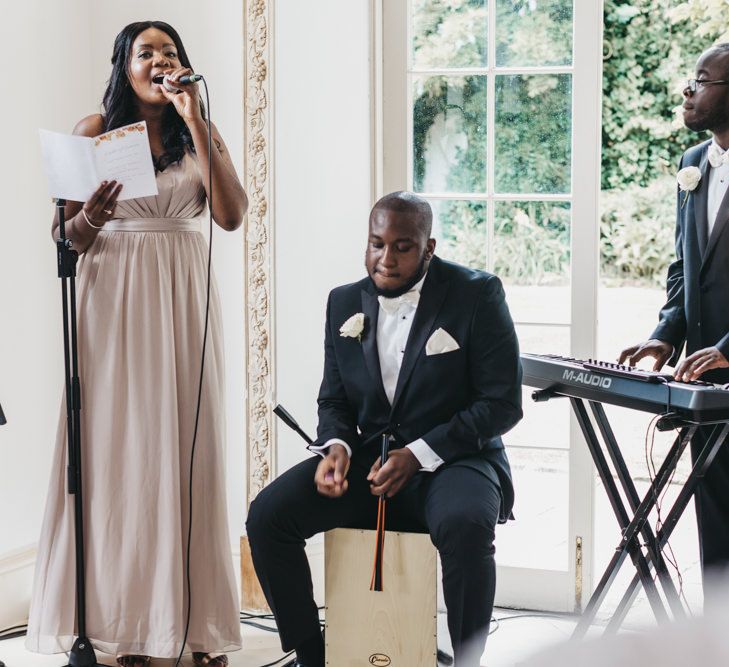 Bridesmaid in a dusky pink dress singing during the Northbrook Park wedding ceremony 