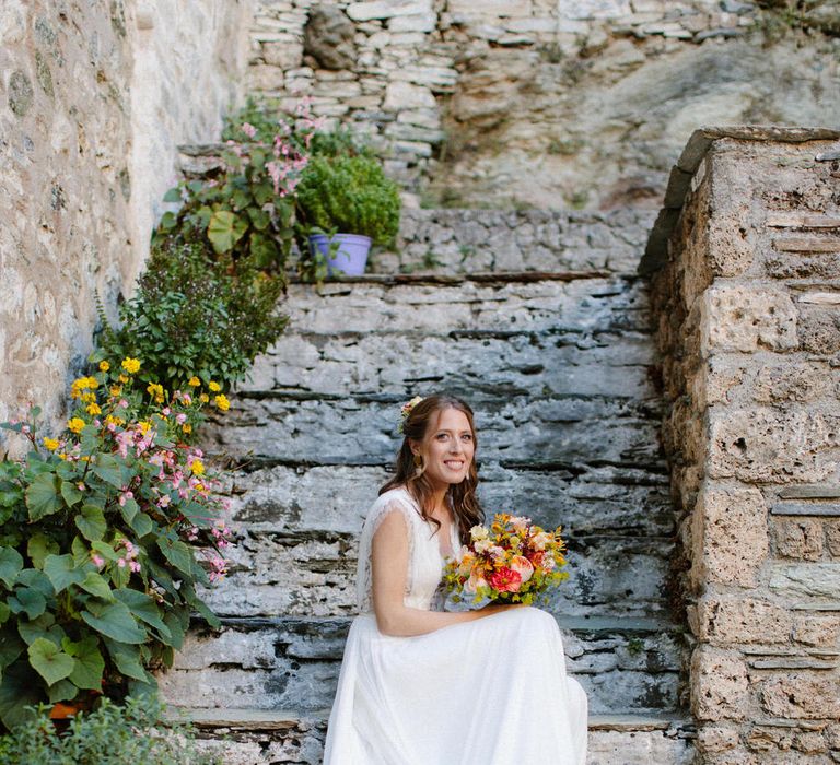 The bride sitting on steps at Valeni Boutique Hotel in Greece wearing Vasia Tzotzopoulou