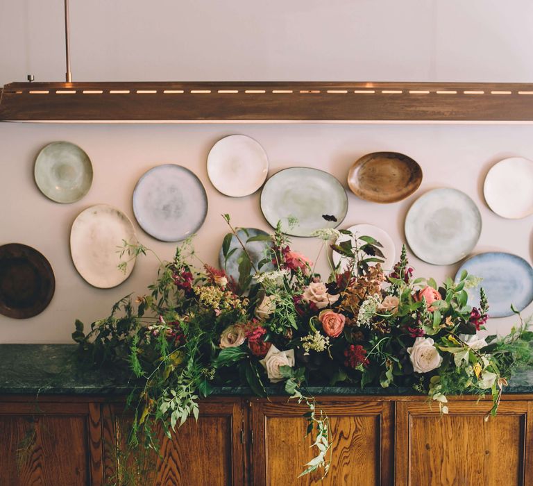 Plate wall with a table in front decorated with a stunning flower installation with bright pink roses 