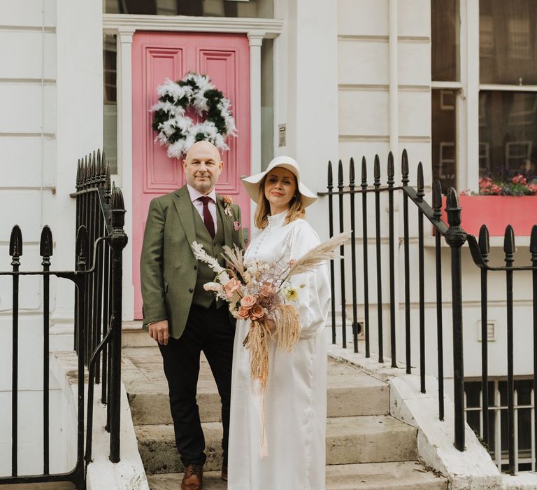 Bride & groom stand in front of pink door with LOVE in the window