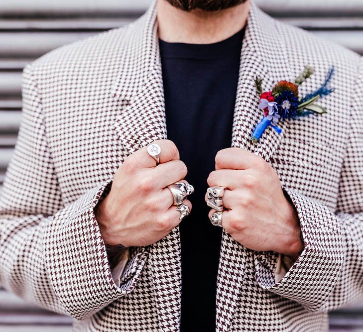 Groom in a dogtooth jacket wearing rings holding onto his lapels 