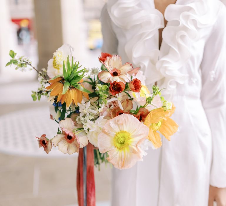 Bride wears ruffled wedding gown with split front and holds floral pastel bouquet 