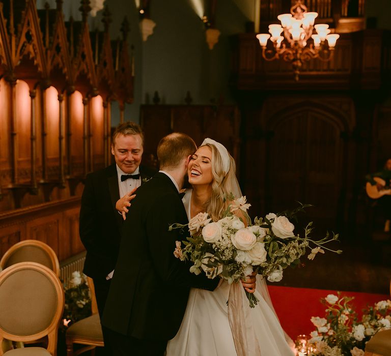 Bride kisses and embraces groom as she reaches the altar with her father on her wedding day